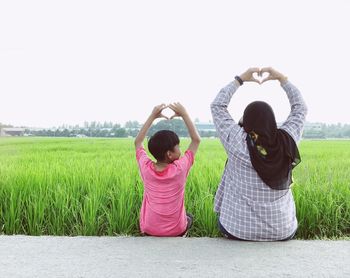 Rear view of mother and son making heart shape while sitting on road against sky