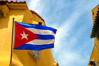 Low angle view of cuban flag and yellow building against sky