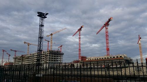 Cranes at construction site against cloudy sky