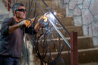 Man wearing protective glasses welds metal with welding machine. sparks from welding fly to sides.