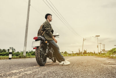 Side view of man leaning on motorcycle at road against sky