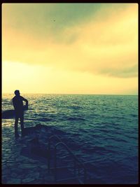 Silhouette man fishing in sea against sunset sky