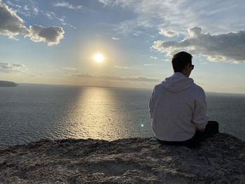 Rear view of man sitting on shore at sunset