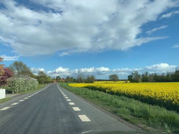 Empty road amidst field against sky