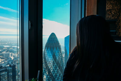 Rear view of woman looking through window in city