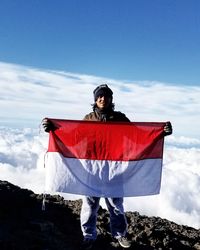 Portrait of young man holding indonesian flag against cloudscape