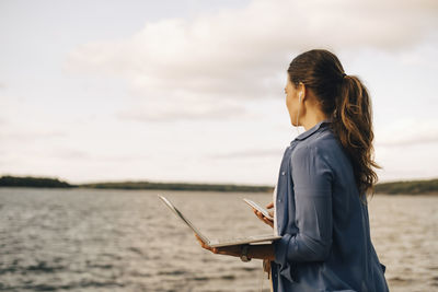 Mature woman using laptop while talking on mobile phone by lake