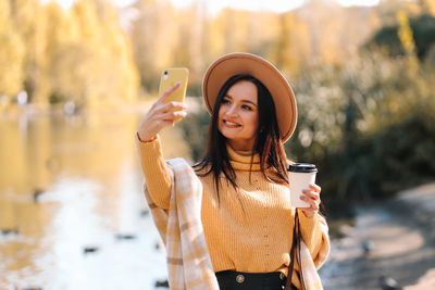 A happy smiling young woman in warm clothes walks in an autumn park in nature in fall