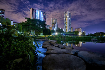 Illuminated buildings by lake against sky at night