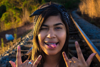 Close-up portrait of smiling young woman sticking out tongue while gesturing horn sign
