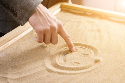 Midsection of person making smiley face on sand
