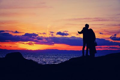 Silhouette man photographing sea against sky during sunset