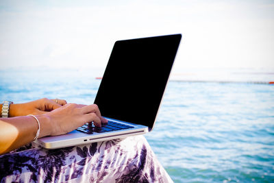 Midsection of person using laptop at sea