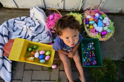 High angle portrait of boy sitting by easter eggs in containers