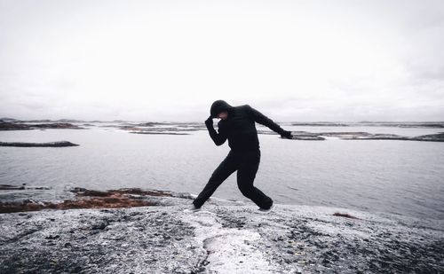 Man wearing costume posing on rock by sea against cloudy sky