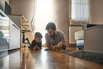 Father and son lying together on the floor playing with toy cars