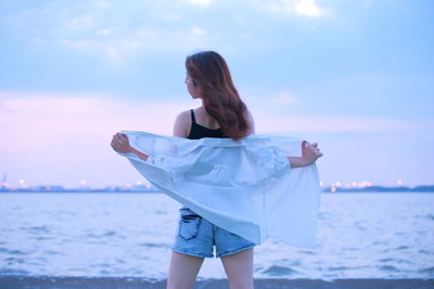 Rear view of woman standing against sea during sunset