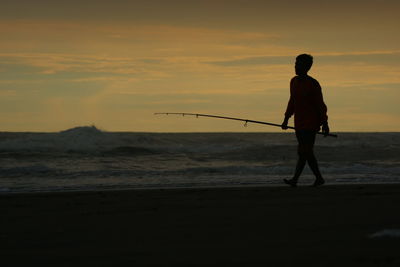 Silhouette man standing on beach against sky during sunset