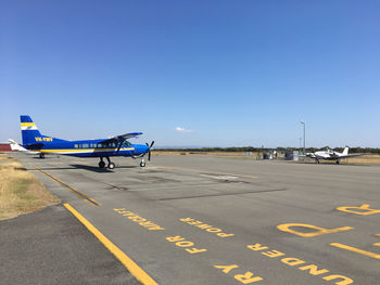 View of airplane on airport runway against clear blue sky