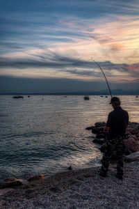 Man fishing in sea against sky during sunset