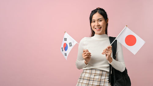 Portrait of young woman holding paper currency against pink background