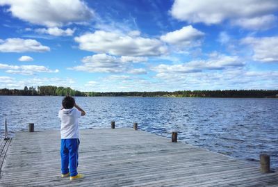 Rear view of boy standing on pier at lake