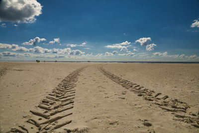 Tire tracks on sand at beach against sky