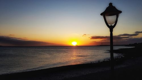 Street light by sea against sky during sunset