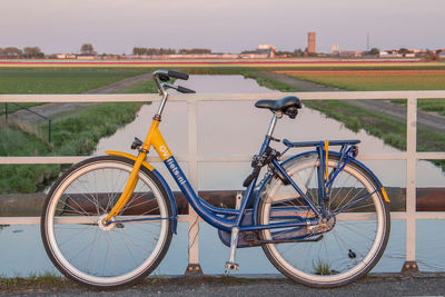 Bicycle parked on field by railing against sky