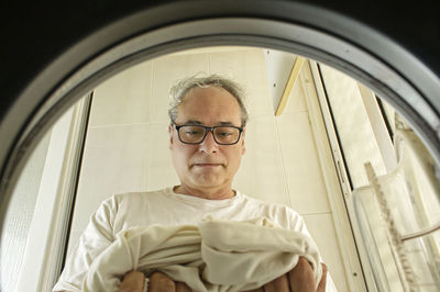 Mature man taking clothes out of the washing machine seen from inside