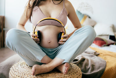 Close-up of a woman holding headphones on her pregnant bare belly.