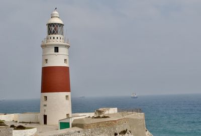 Lighthouse amidst sea and buildings against sky