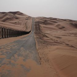 Country road by fence against sky at desert