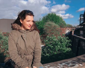 Portrait of smiling young woman standing by plants against sky