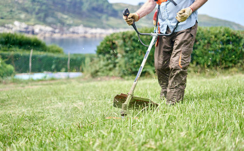 Crop elderly man mowing grass in backyard with lawn mower in lakeside