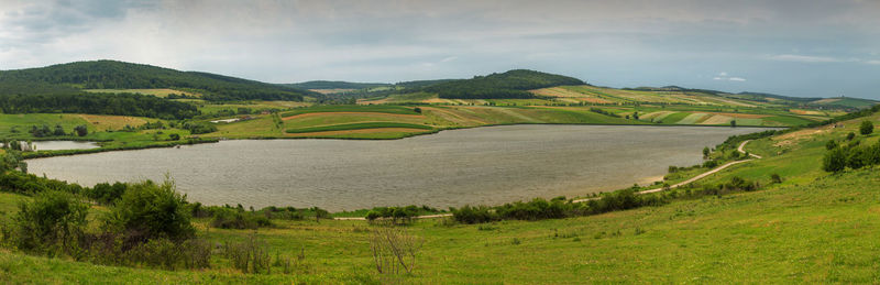 Scenic view of green landscape and river against sky