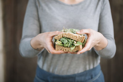 Midsection of woman holding sandwich while standing at home