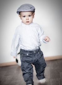 Portrait of boy wearing flat cap walking against wall at home