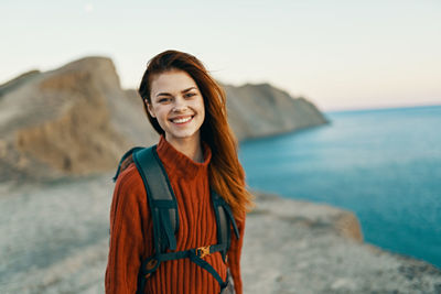 Portrait of smiling young woman standing against sea