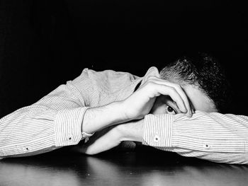 Close-up of man covering face on table against black background