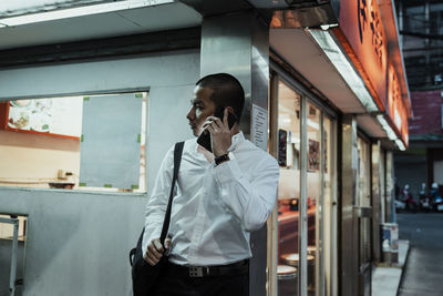 Businessman talking over smart phone while standing against wall