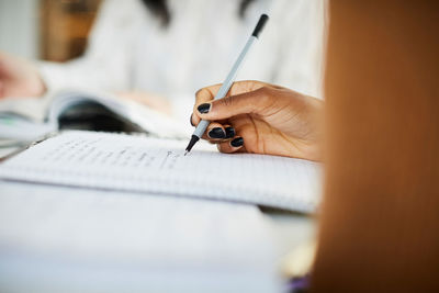 Cropped hand of woman writing on book while studying at table