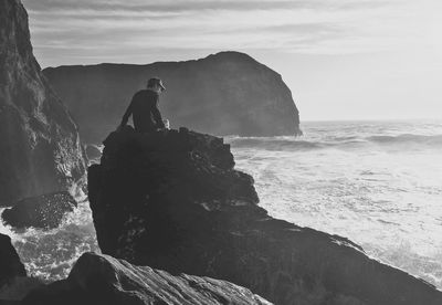 Rear view of young man standing on cliff by sea against sky