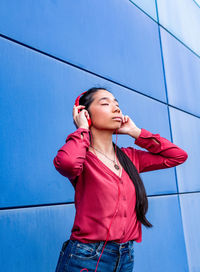 Low angle view of young woman looking away against blue wall