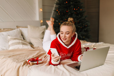 Smiling woman using mobile phone while lying on bed at home