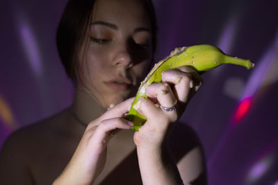 Young woman squeezing banana against wall