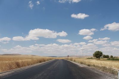 Empty road amidst field against sky