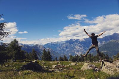 Woman with arms raised on mountain against sky