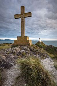 Cross on rocky shore against cloudy sky