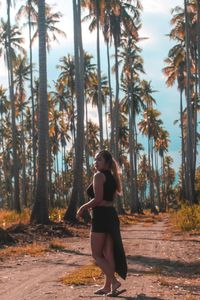 Portrait of young woman standing on dirt road against palm trees